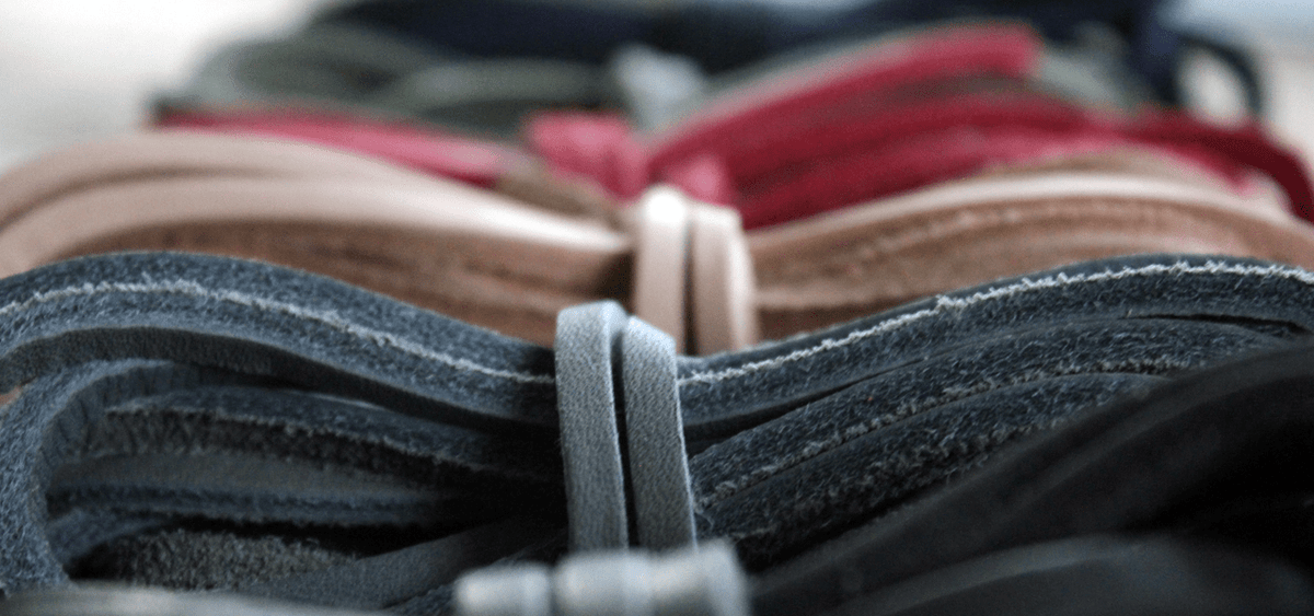 Close-up of coiled flat waxed cotton boot laces in several colors, including denim grey, tan, pink, and olive.
