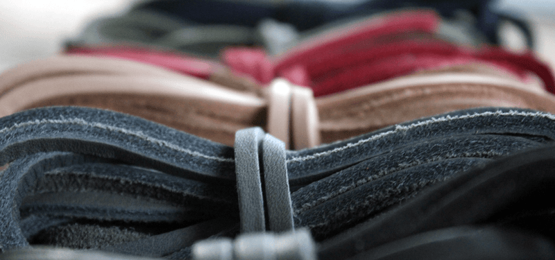 Close-up of coiled flat waxed cotton boot laces in several colors, including denim grey, tan, pink, and olive.