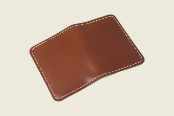 Warden bifold wallet in amaretto Horween shell cordovan, chestnut exterior laid open, cream backdrop