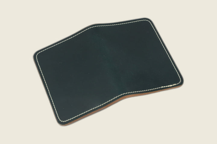 Warden bifold wallet in dark green Horween shell cordovan, deep forest exterior, cream backdrop