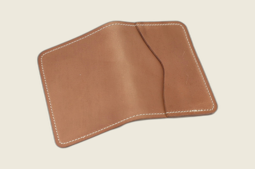 Warden bifold wallet in pale unglazed natural shell cordovan, open showing curved slip pocket, cream backdrop