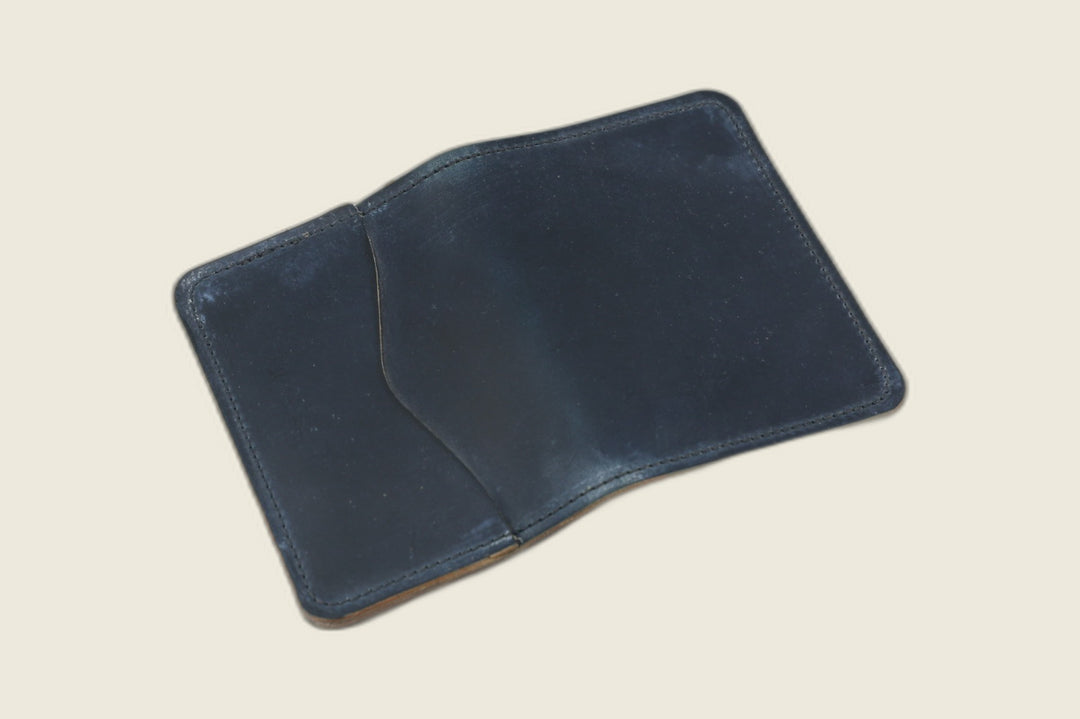 Warden bifold wallet in navy Rocado shell cordovan, matte blue exterior with slip pocket, cream flat lay