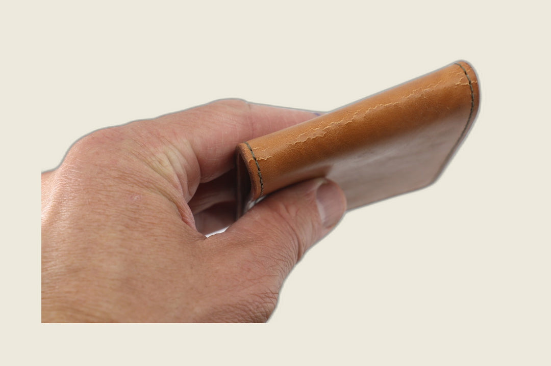 Stronghold bifold in tan 1940s calfskin folded closed, held in hand showing creased spine grain