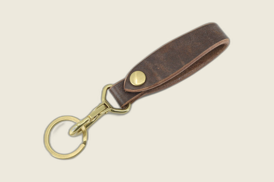 Lanyard in brown J&FJ harness leather with brass snap, swivel clasp and split key ring, cream backdrop