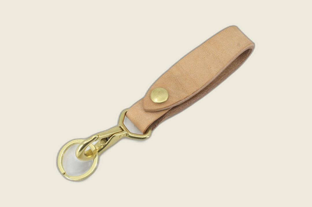 Lanyard in natural J&FJ harness leather with brass snap, swivel snap hook and key ring, flat lay on cream backdrop