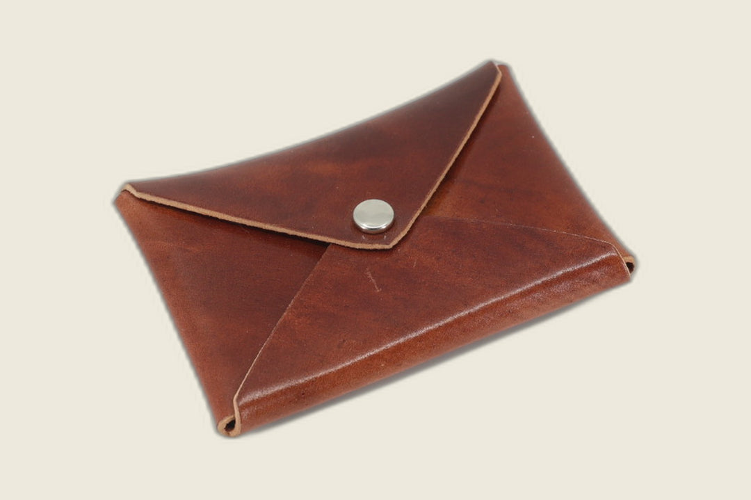 Aegis envelope card wallet in Rocado marbled red shell cordovan with nickel snap, closed at an angle on a cream backdrop