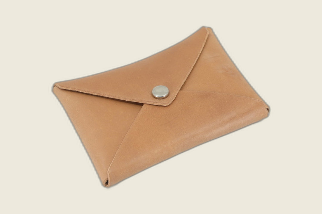 Aegis envelope card wallet in Comipel natural shell cordovan, nickel snap closure, angled flat lay on cream background