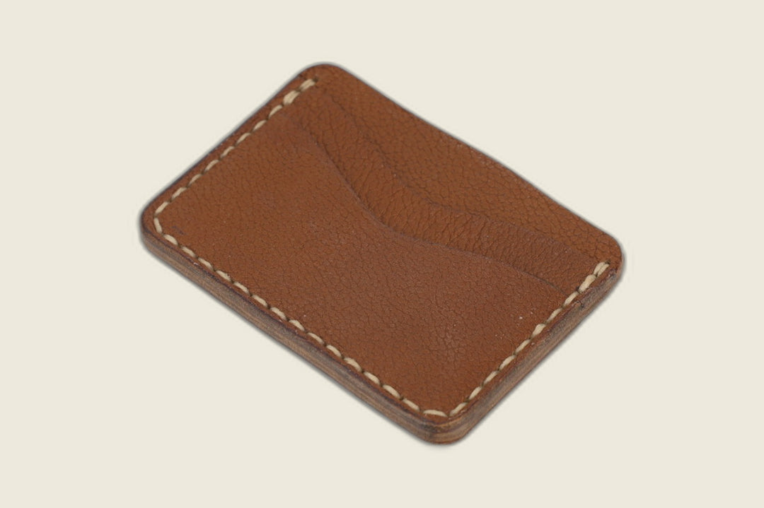 Buckler four-slot card holder in cognac calfskin with cream saddle stitching, front slots shown at an angle