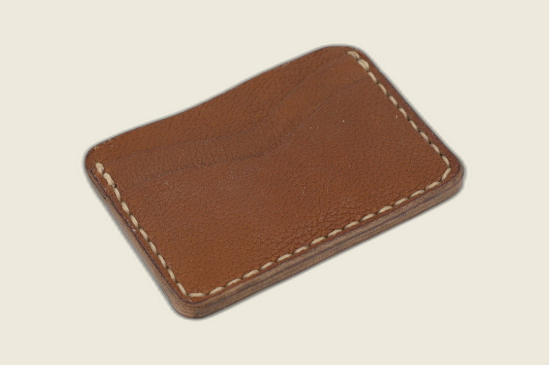 Reverse of the Buckler cognac calfskin card holder with one curved slot and cream stitching on a cream backdrop