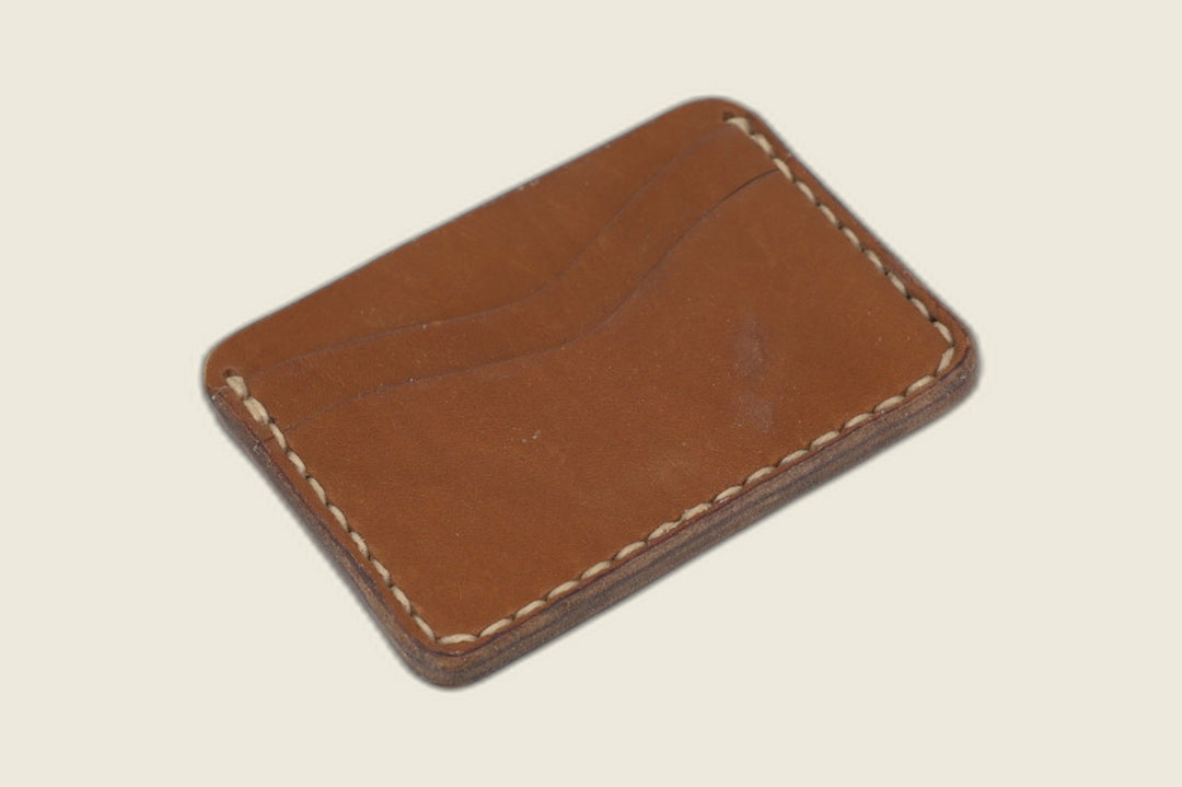 Buckler four-slot card holder in Haas caramel calfskin with cream saddle stitching, twin curved slots facing up