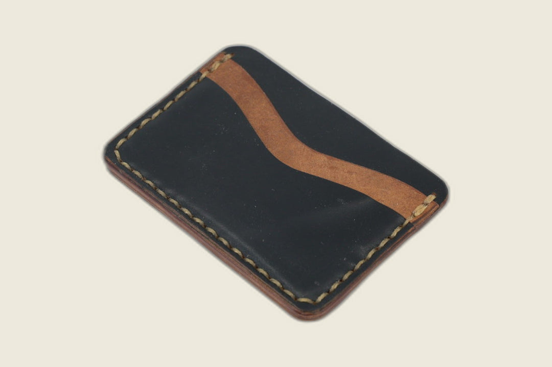 Reverse of the Buckler black horsebutt card holder, tan curved slot trim against black leather, angled flat lay