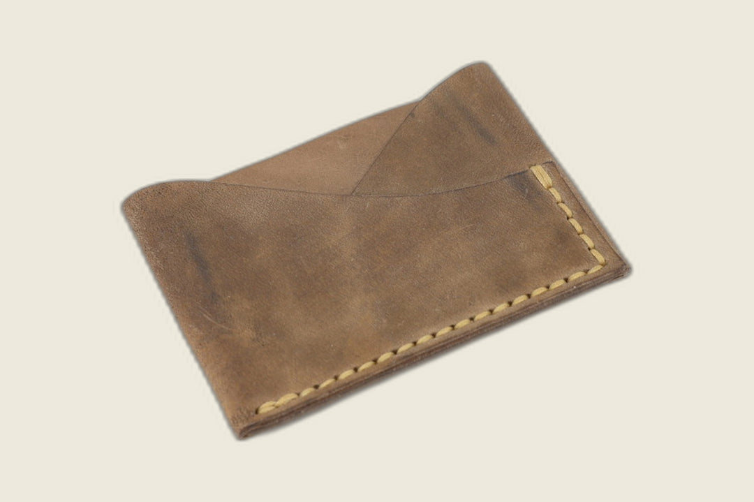 Sentinel card sleeve in matte Maryam fango horsebutt, crossed peak pockets with yellow stitching, angled on cream