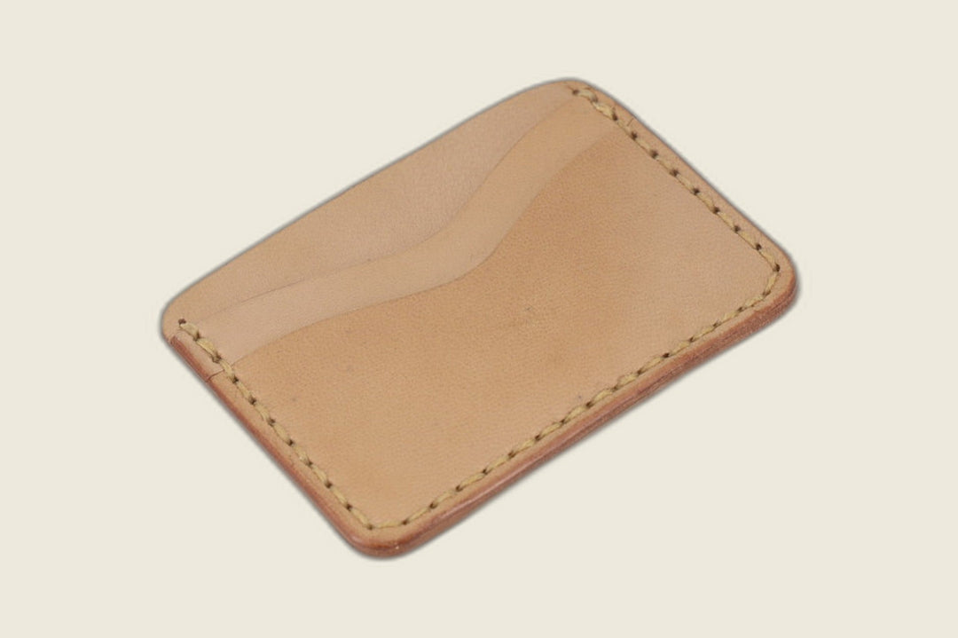 Buckler four-slot card holder in undyed natural goat, twin curved slots with tonal stitching, angled flat lay